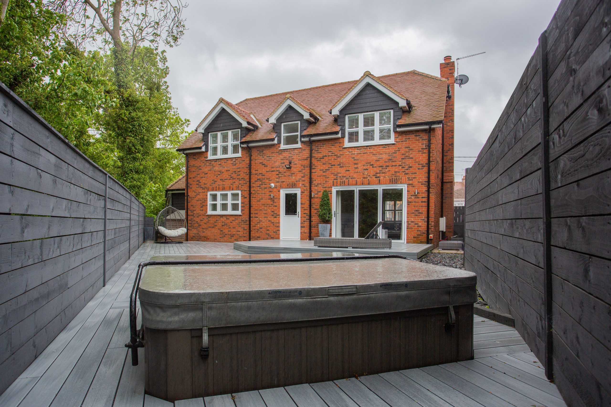Backyard of a modern brick suburban home with a hot tub on the patio, ideal for a New Jersey property