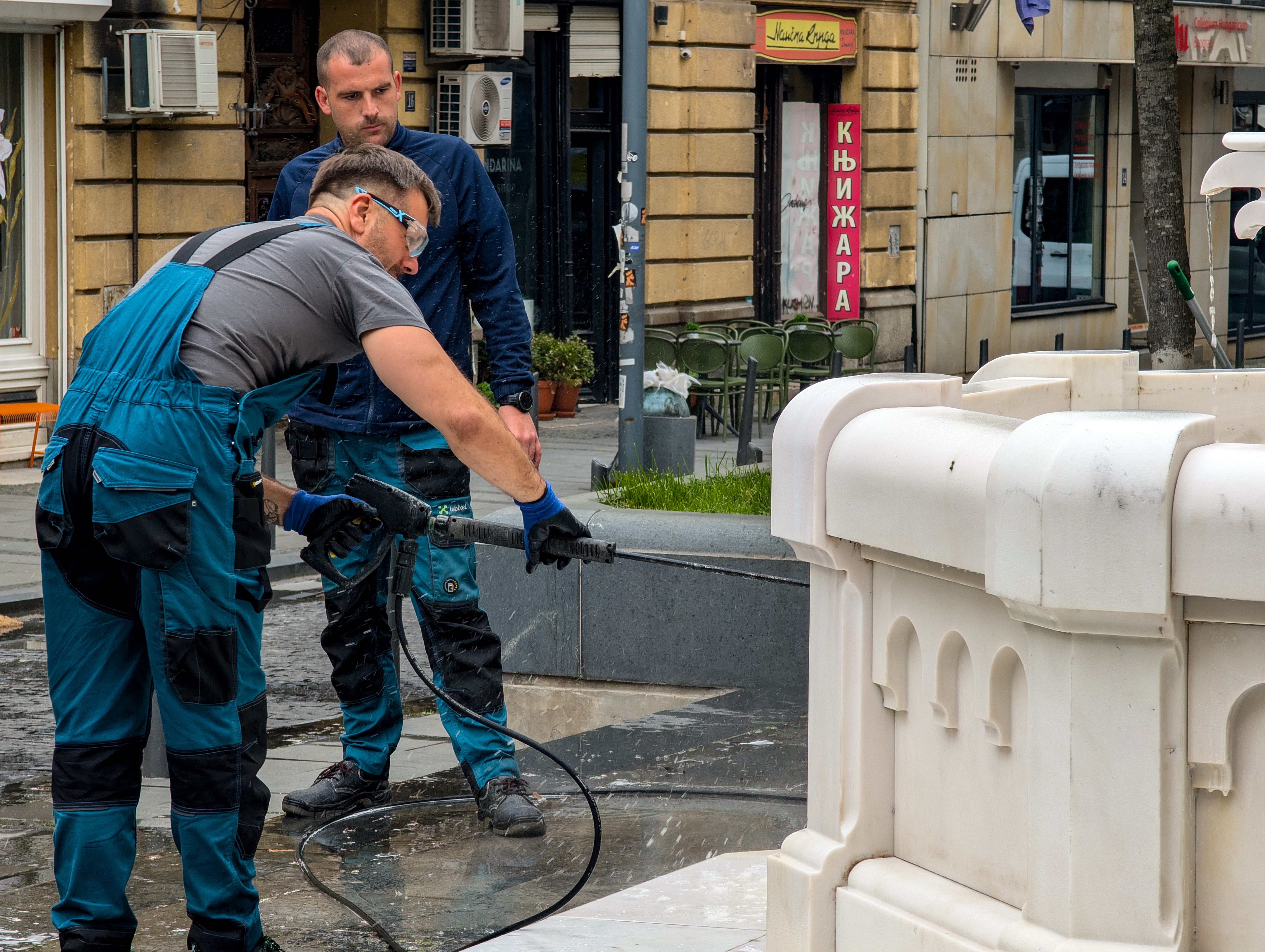 Two workers cleaning a commercial fountain with a pressure washer in an urban setting
