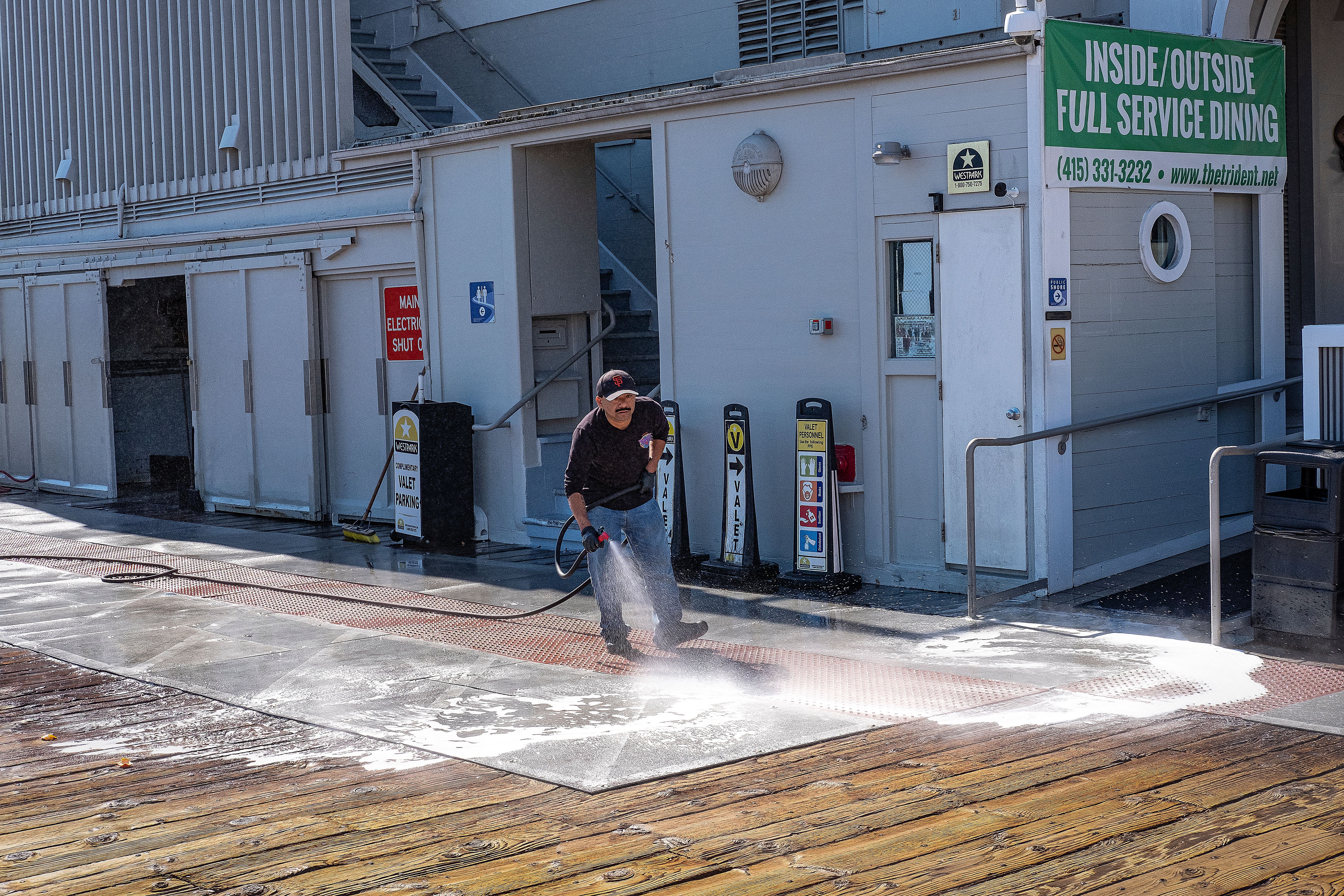 Worker using a pressure washer to clean a commercial sidewalk outside a building