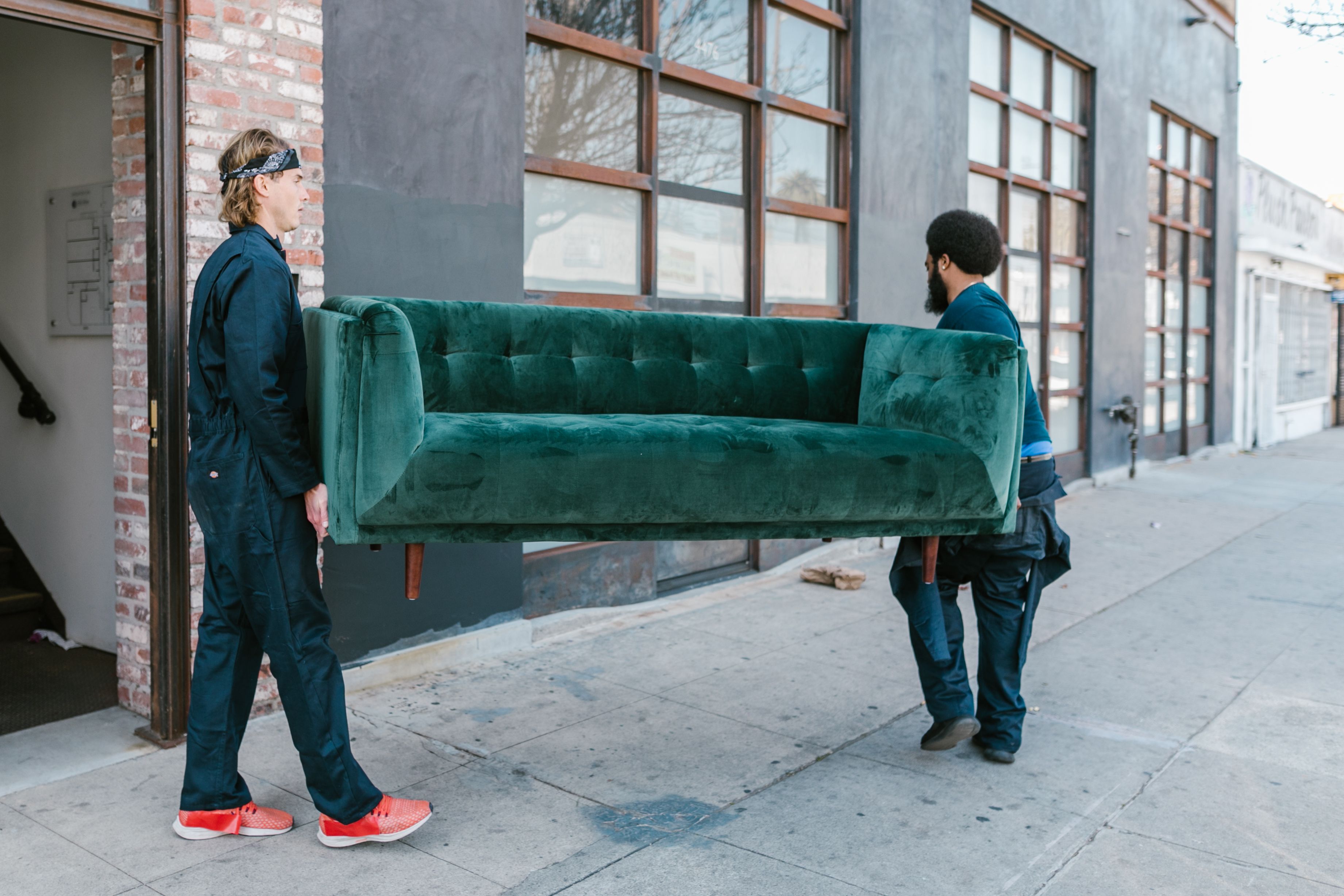 Two professional movers carrying a green sofa out of a property during a furniture removal