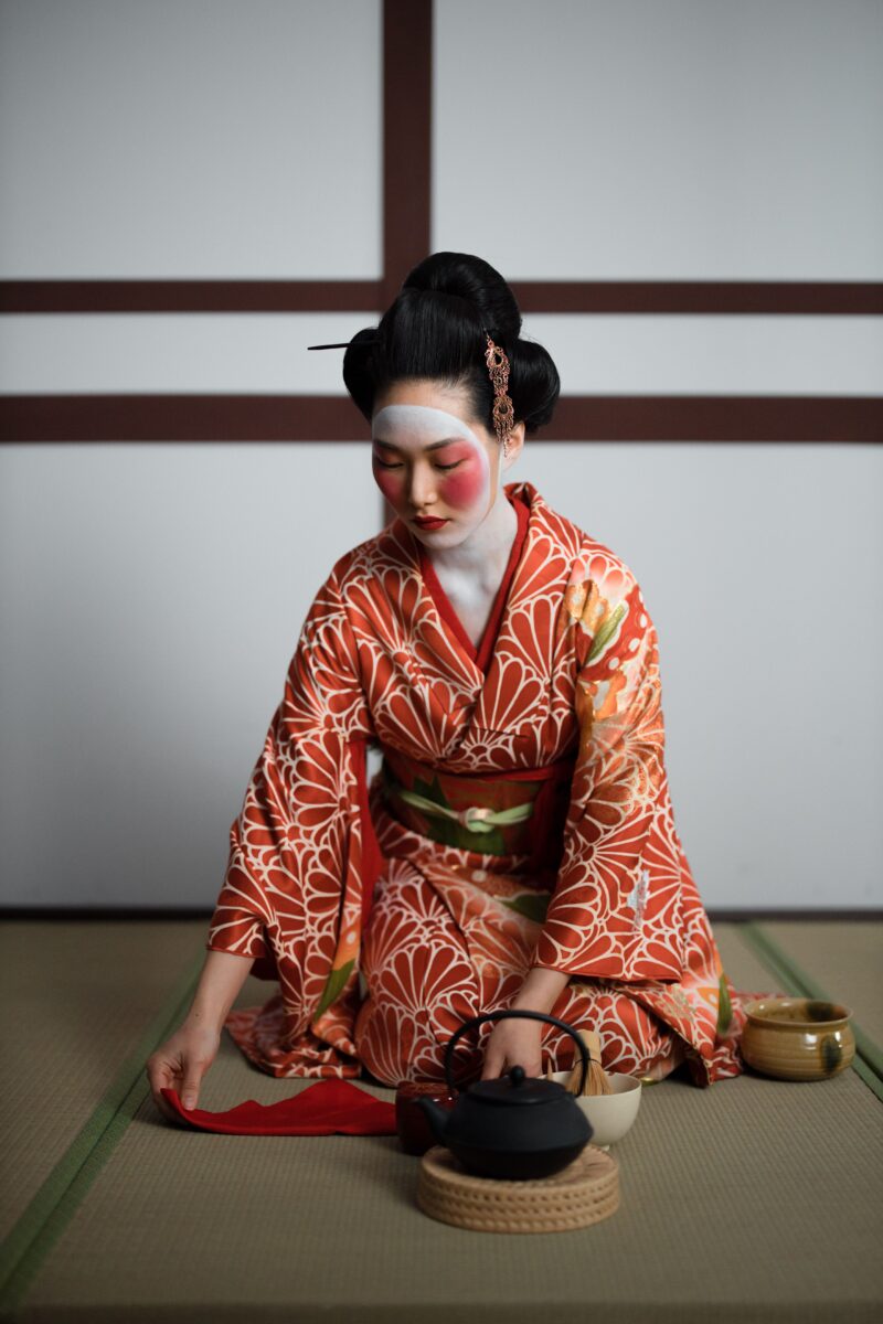 A geisha in a kimono performing a traditional Japanese tea ceremony indoors