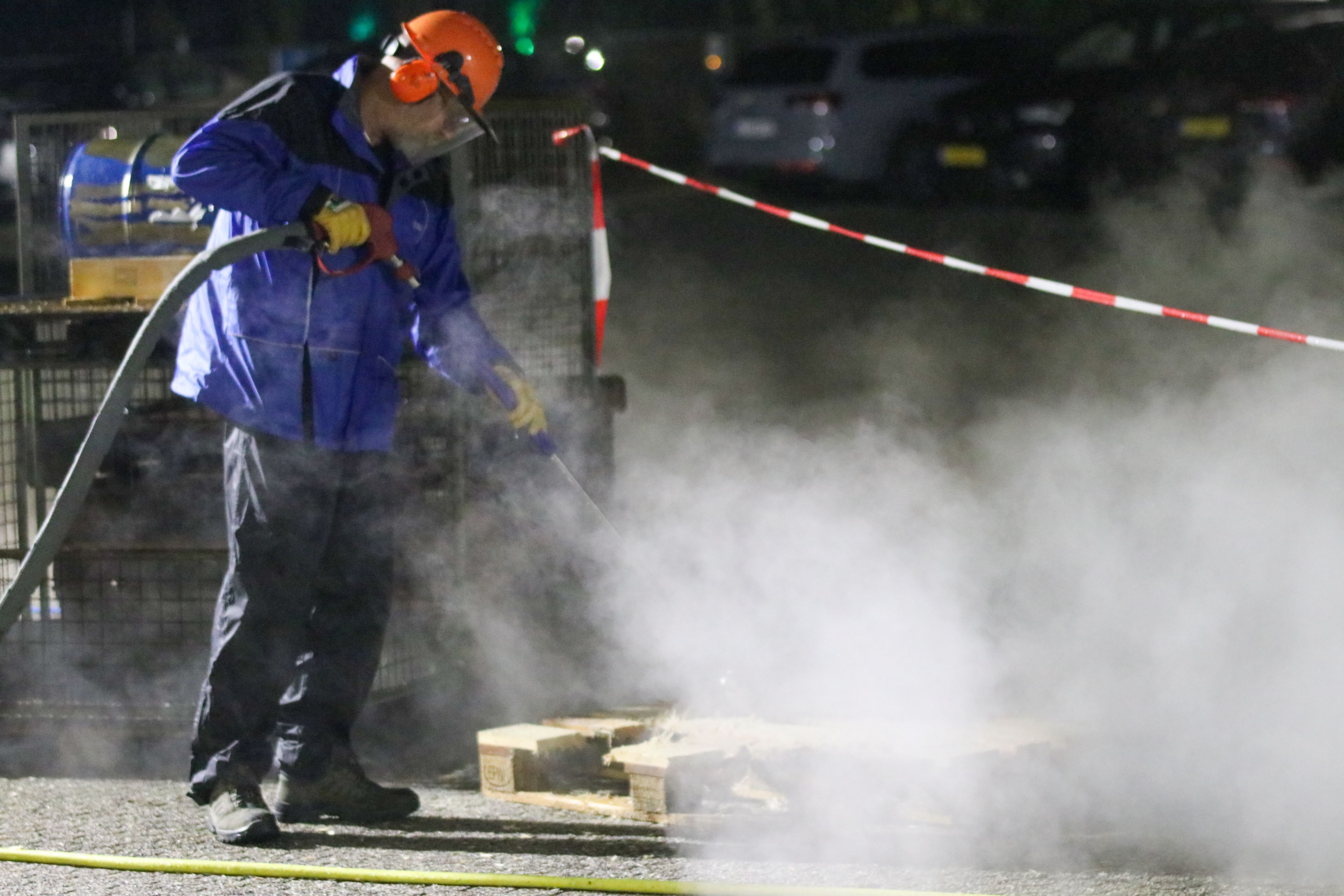 Man in protective gear using a high-pressure washer amid steam in an industrial setting
