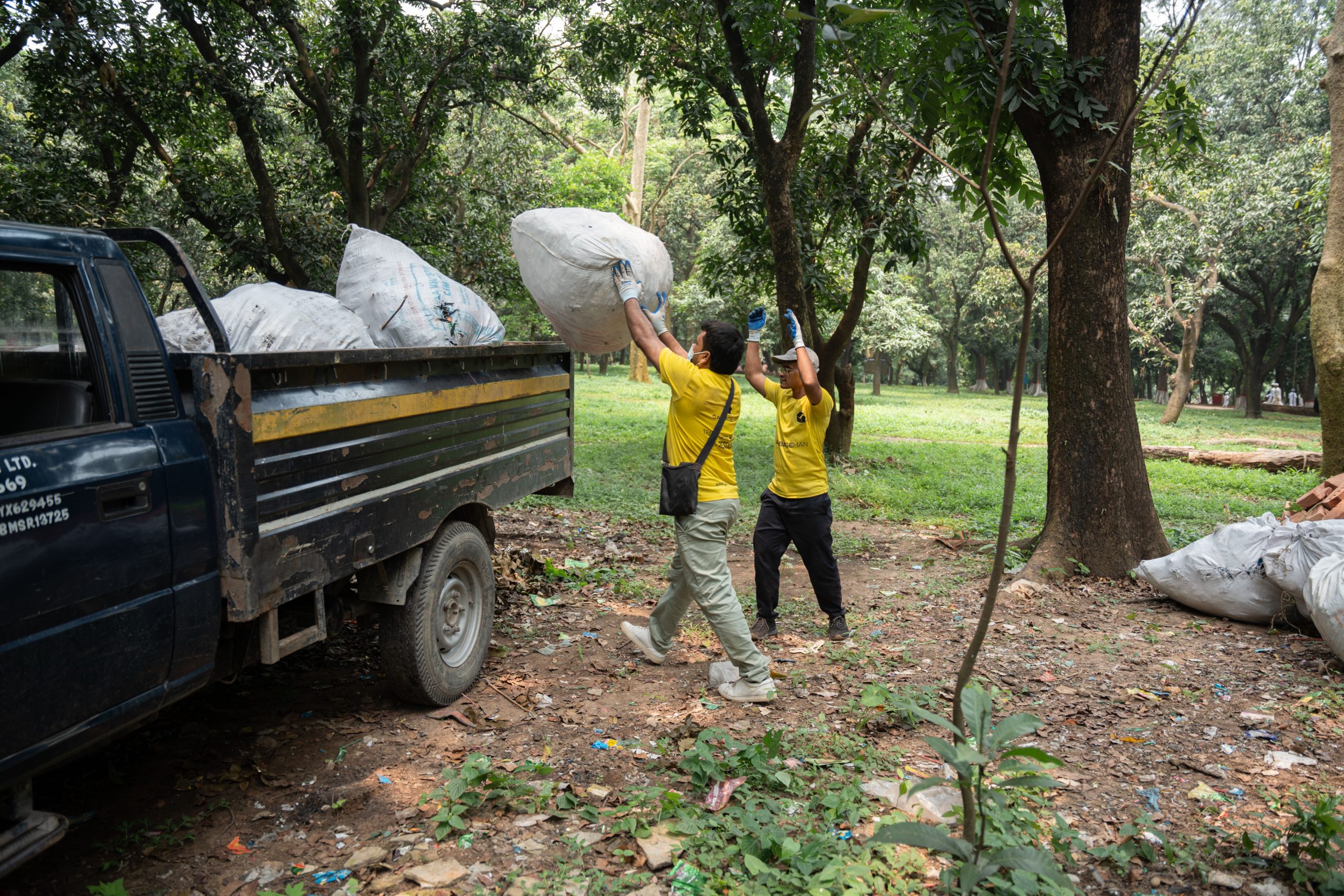 Two workers in yellow shirts loading large garbage bags into a junk removal truck