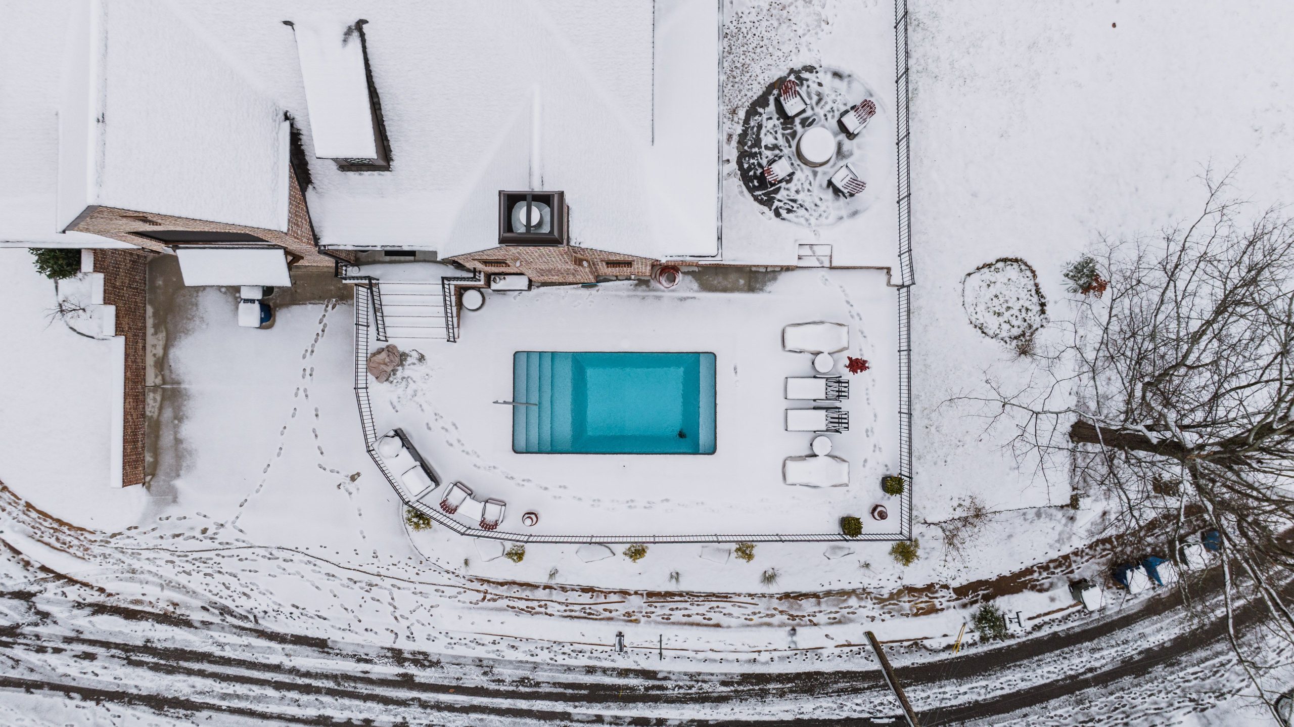 Aerial view of a backyard swimming pool protected with a safety cover under winter snow