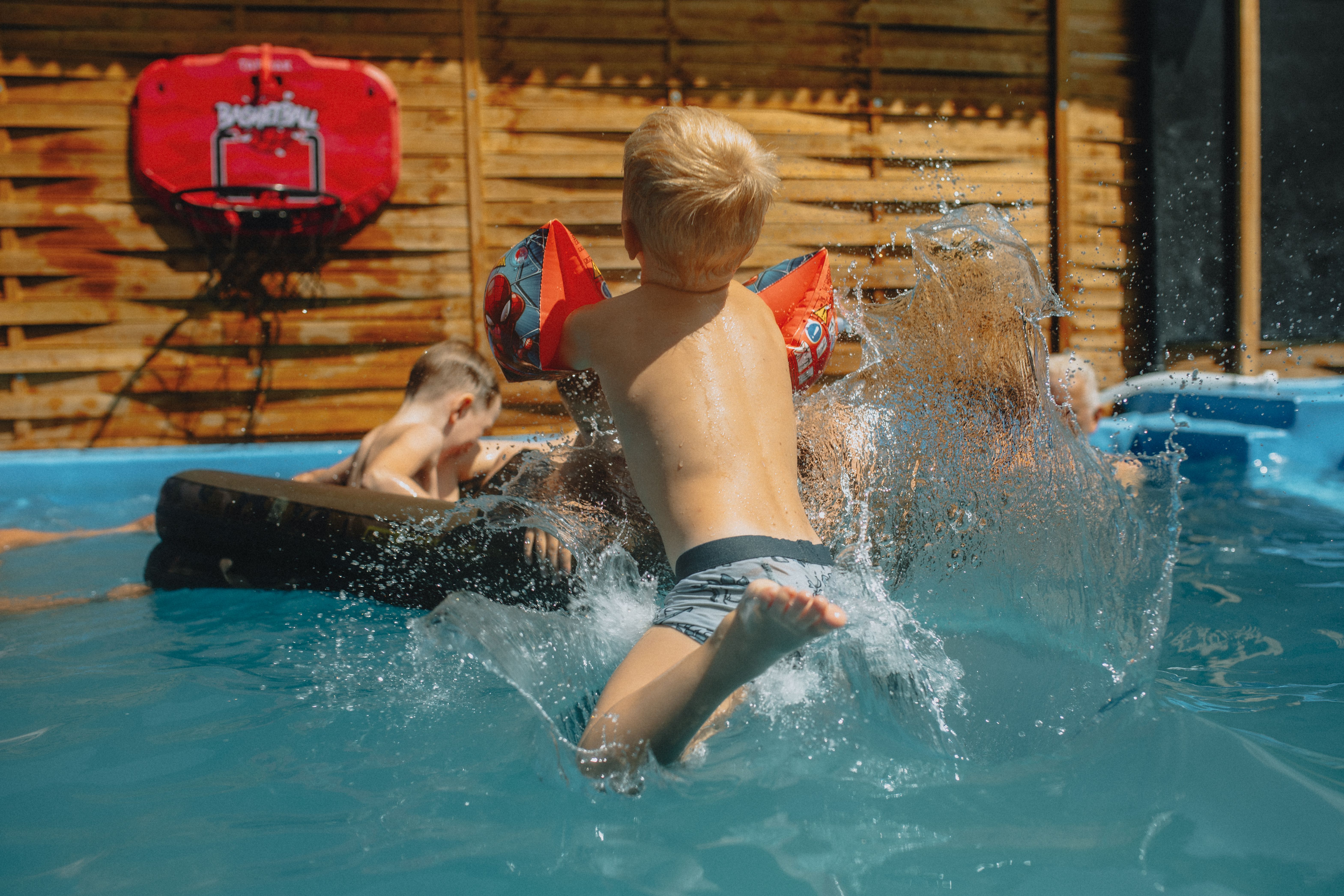 Children playing in an outdoor swimming pool on a sunny day, highlighting the need for pool safety