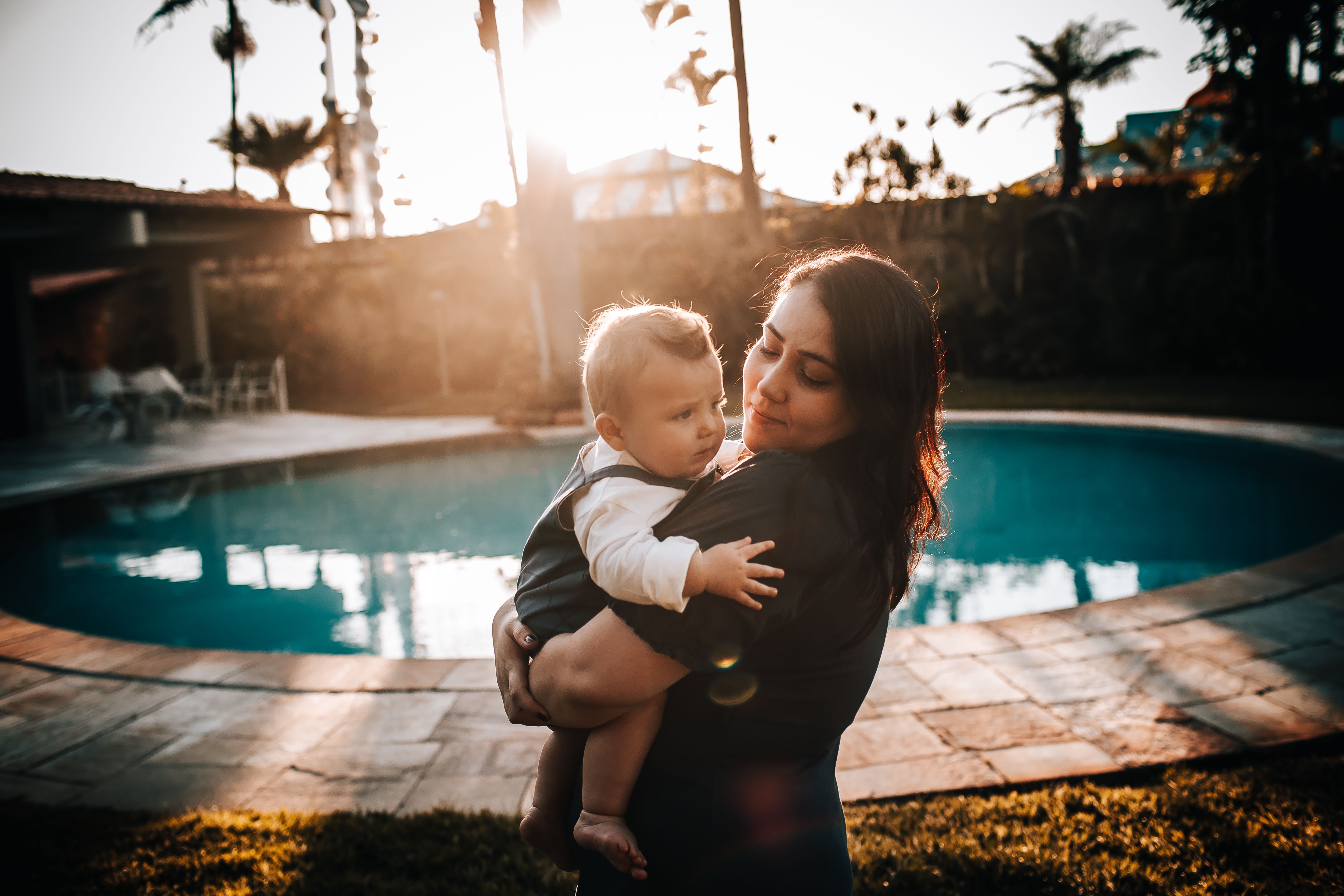 Parent holding a baby beside a backyard pool at sunset highlighting pool safety