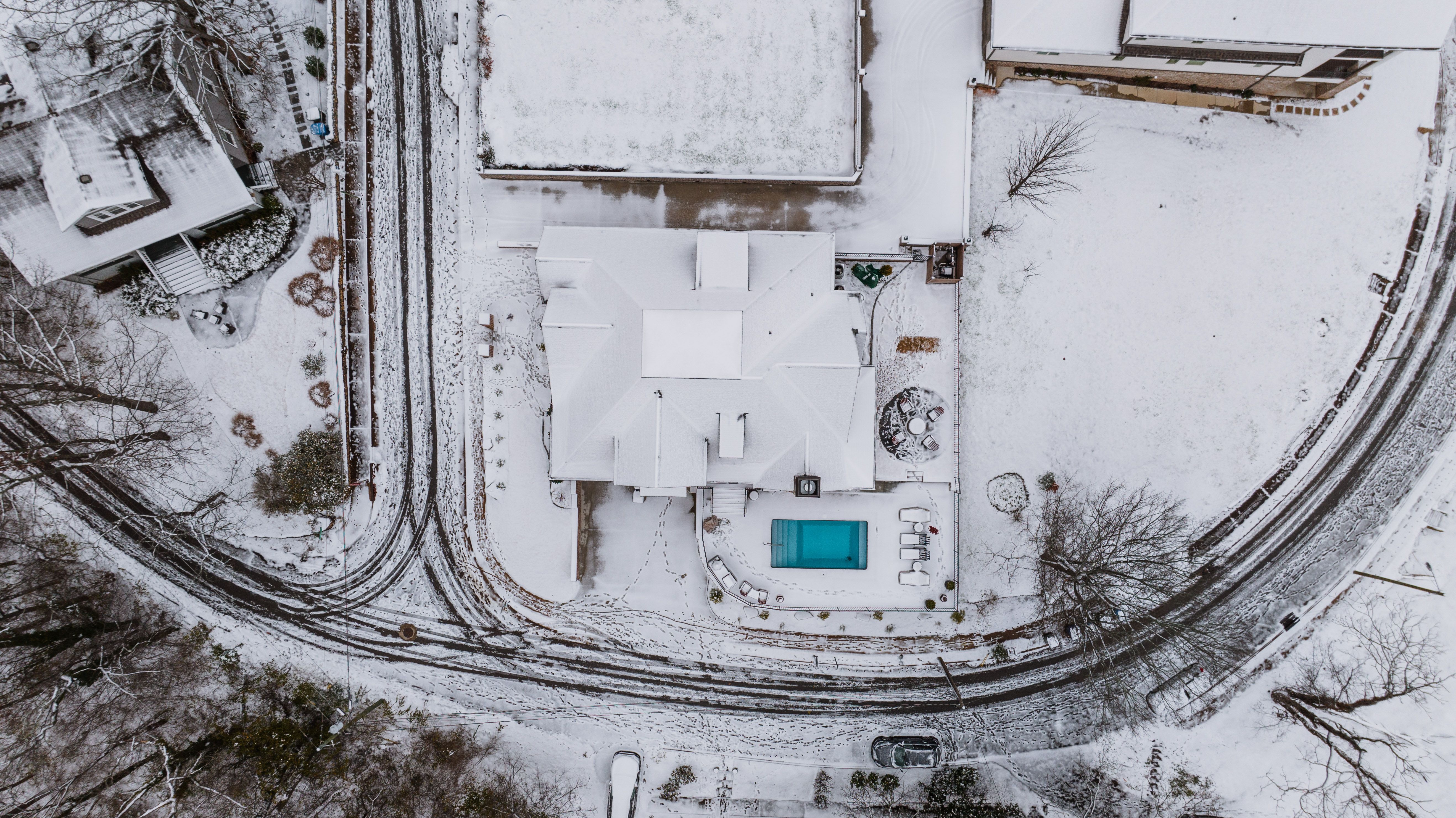 Aerial view of a snow-covered suburban neighborhood with houses and a protected swimming pool