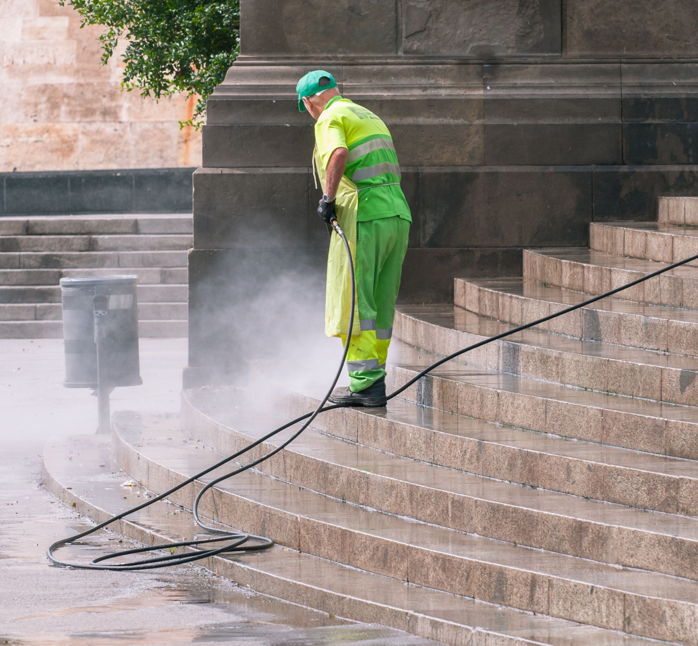 Worker pressure washing stone steps and hardscape in an outdoor public area