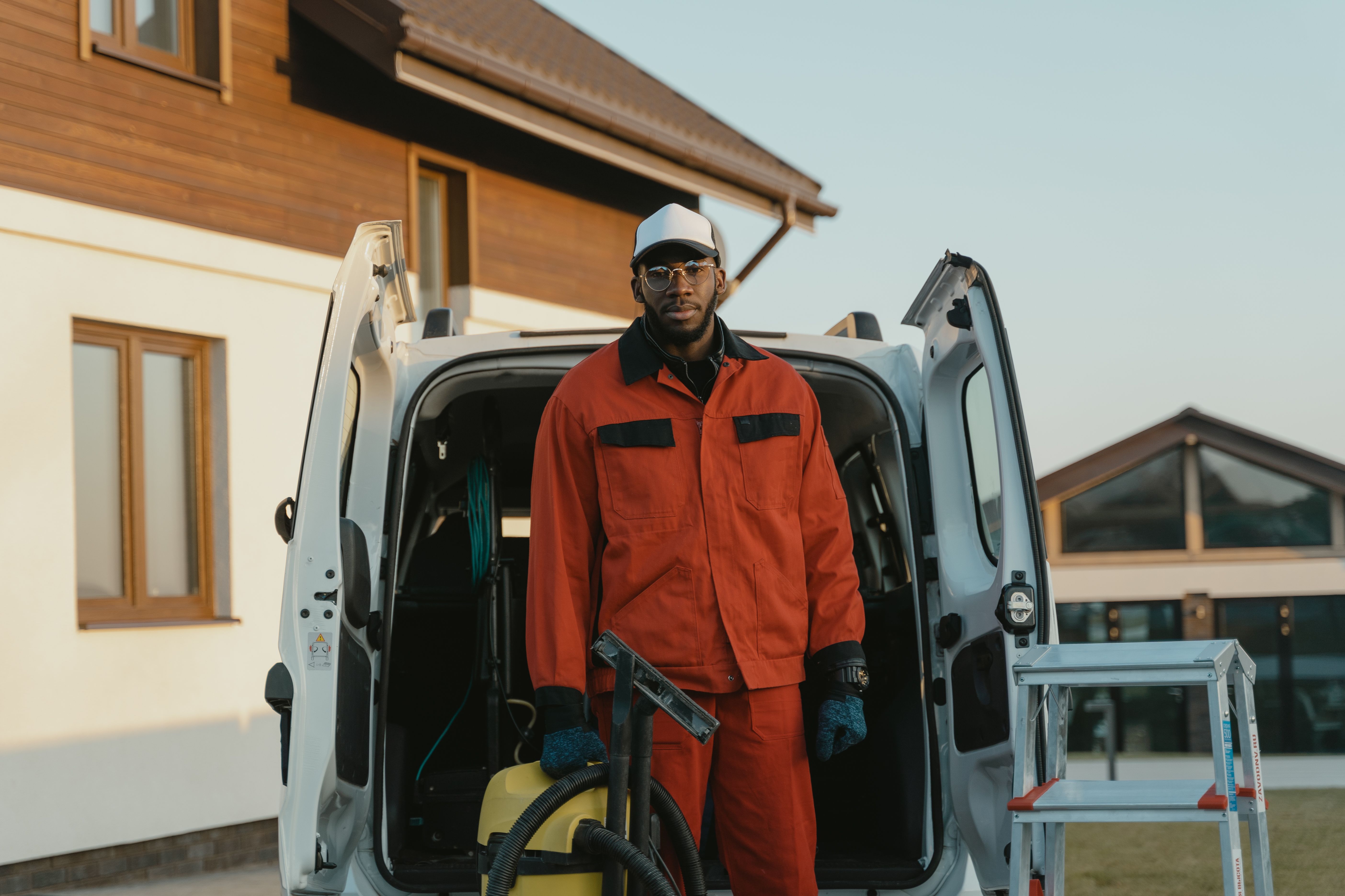Professional in workwear standing with cleaning equipment beside a service van outside a building