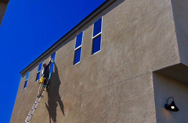 Professional window cleaner using a ladder to wash the exterior windows of a building