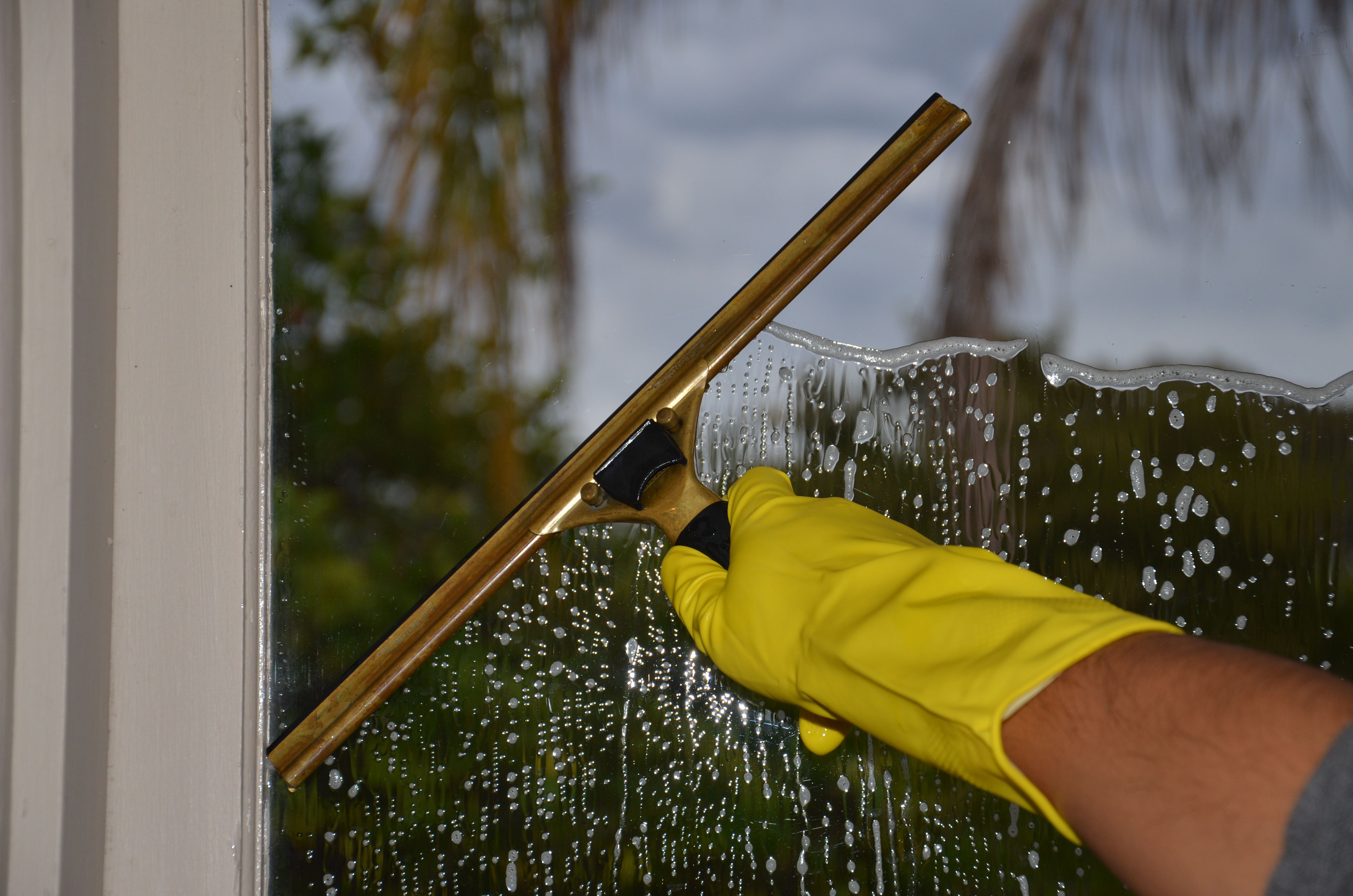 Hand wearing a glove cleaning a window with a squeegee